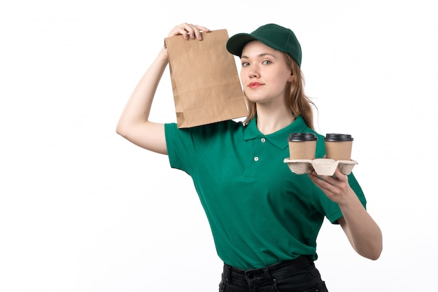 フードパッケージとコーヒーカップを保持している笑顔の緑の制服を着た正面若い女性宅配便