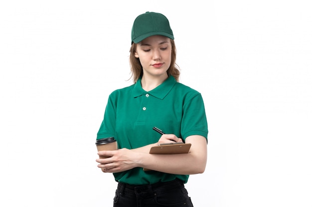 A front view young female courier in green uniform smiling holding notepad and coffee cup