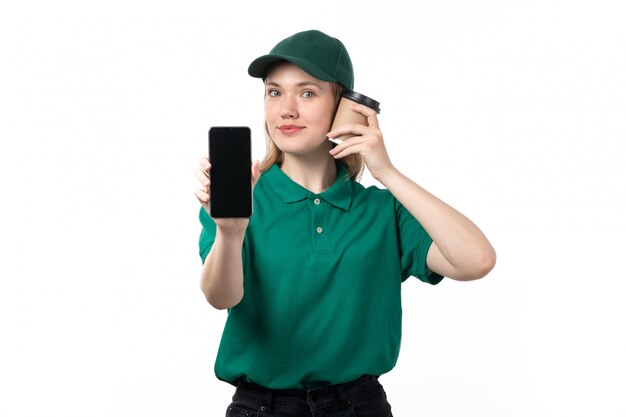Молодая женщина-курьер в зеленой форме, улыбаясь, держит смартфон и чашку кофе, вид спереди