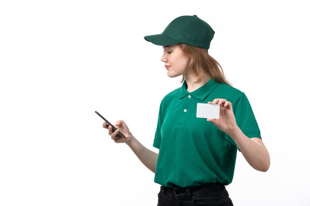 Молодая женщина-курьер в зеленой форме, улыбаясь, держит смартфон и белую карточку, вид спереди