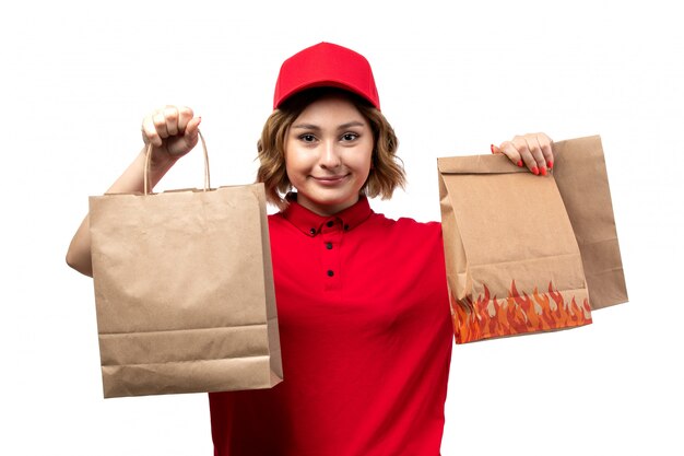 배달 패키지를 들고 빨간 셔츠 빨간 모자에 전면보기 젊은 여성 택배 제공하는 흰색 배경 유니폼 서비스에 미소