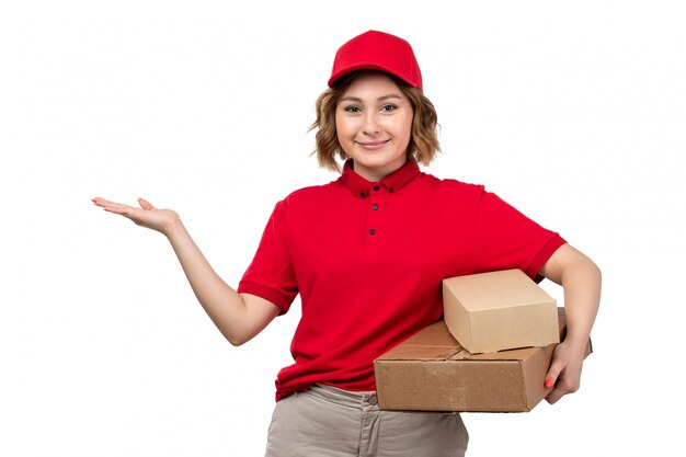 Молодая женщина-курьер в красной рубашке с красной кепкой, держащая посылки с доставкой, улыбается