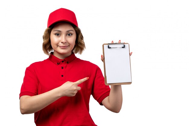 A front view young female courier in red shirt red cap holding notepad smiling