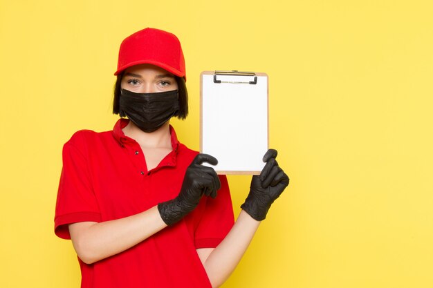 A front view young female courier in red uniform black gloves black mask and red cap holding notepad