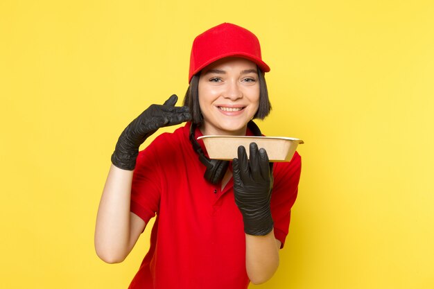 A front view young female courier in red uniform black gloves and red cap holding food bowl