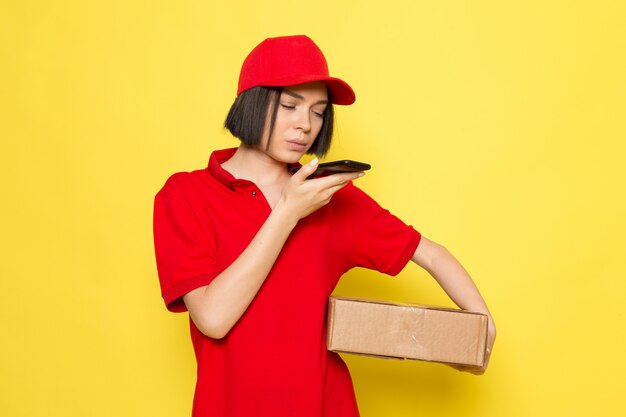 赤い制服の黒い手袋と赤い帽子フードボックスを押しながら電話で話している正面若い女性宅配便