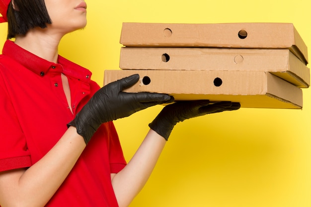 Un corriere femminile giovane di vista frontale in guanti neri uniformi rossi e spiritello malevolo che tengono le scatole di alimento