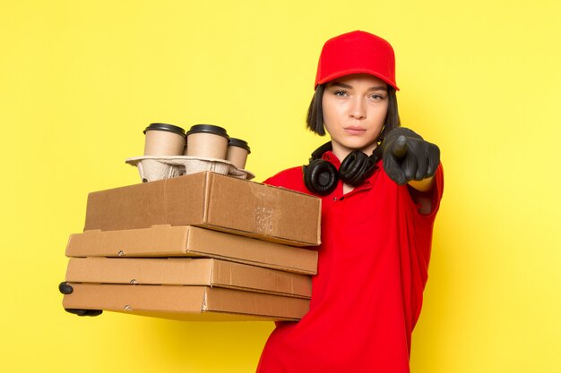 A front view young female courier in red uniform black gloves and red cap holding food boxes