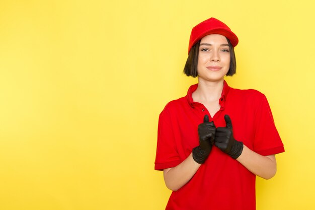 A front view young female courier in red uniform black gloves and red cap posing with smile