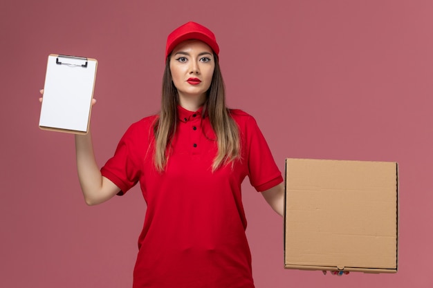 분홍색 배경 배달 서비스 유니폼 회사 작업에 메모장 배달 음식 상자를 들고 빨간 제복을 입은 전면보기 젊은 여성 택배