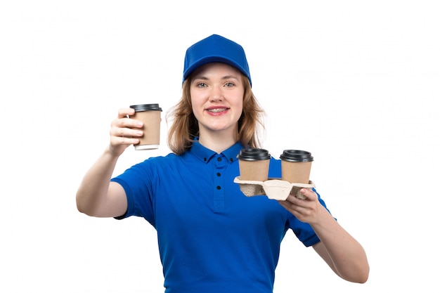 Молодая женщина-курьер в униформе, держащая кофейные чашки улыбается, вид спереди