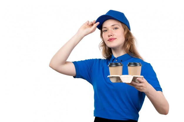 Молодая женщина-курьер в униформе, держащая чашки кофе улыбается, вид спереди
