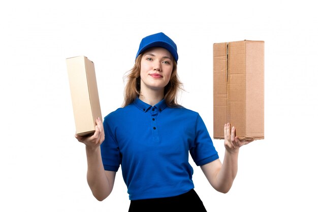 A front view young female courier in uniform holding delivery packages smiling