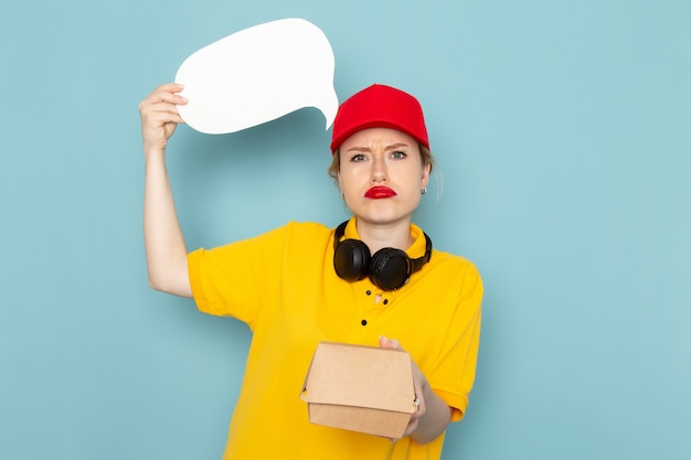 Foto gratuita giovane corriere femminile di vista frontale in camicia gialla e mantello rosso che tiene il pacchetto alimentare e segno bianco sullo spazio blu