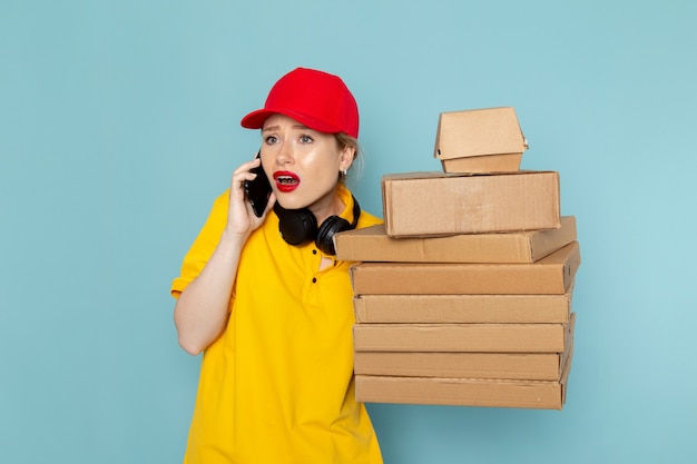 黄色のシャツと赤いマントの青い宇宙の仕事に乗算パッケージを保持している正面の若い女性宅配便