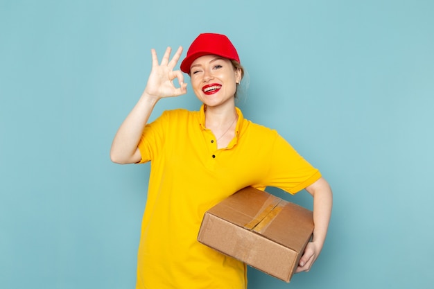 Молодая женщина-курьер в желтой рубашке и красной накидке, держащая пакет на синей космической работе, вид спереди