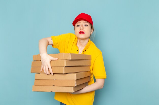 Foto gratuita giovane corriere femminile di vista frontale in camicia gialla e mantello rosso che tiene i pacchetti sul lavoro dello spazio blu