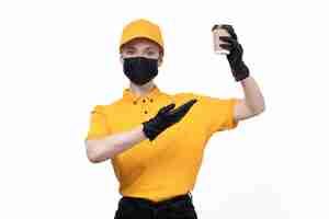 Free photo a front view young female courier in yellow uniform black gloves and black mask holding coffeee cup