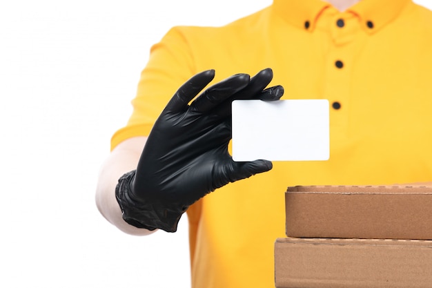 黄色の制服の黒い手袋とピザの箱を押しながら白いカードを保持している黒いマスクの正面の若い女性の宅配便