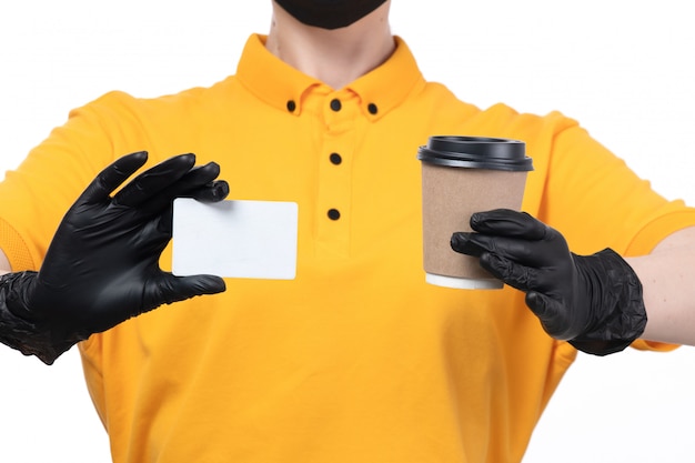 노란색 유니폼 검은 장갑과 흰색 카드와 커피 컵을 들고 검은 마스크에 전면보기 젊은 여성 택배