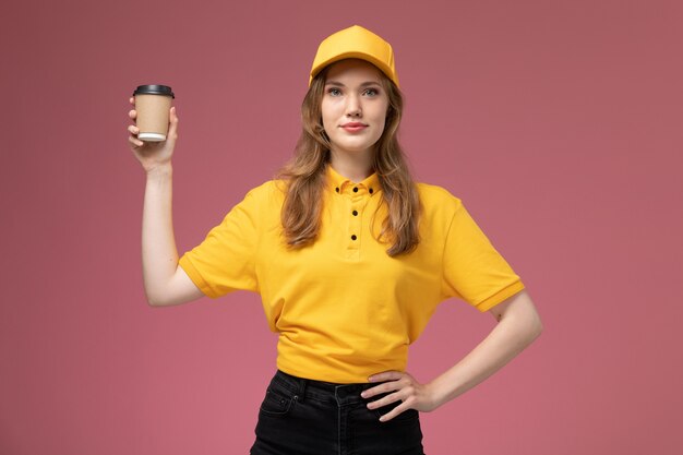 Вид спереди молодая женщина-курьер в желтой форме с пластиковой доставкой кофе на розовом столе работник службы доставки униформы