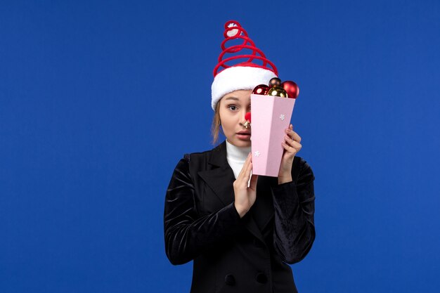Вид спереди молодая женщина закрыла лицо игрушками на синей стене эмоции новогоднего праздника