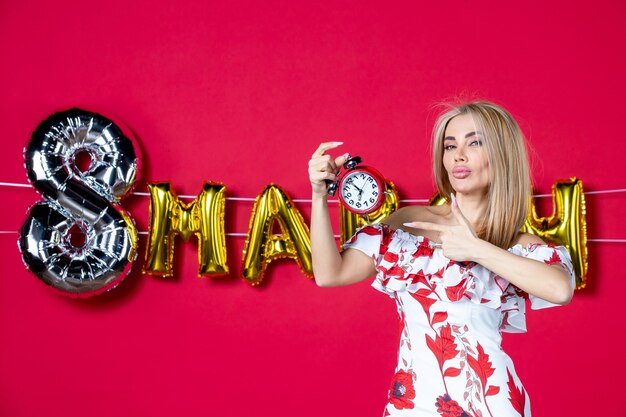 Front view young female in cute dress holding clock on red time