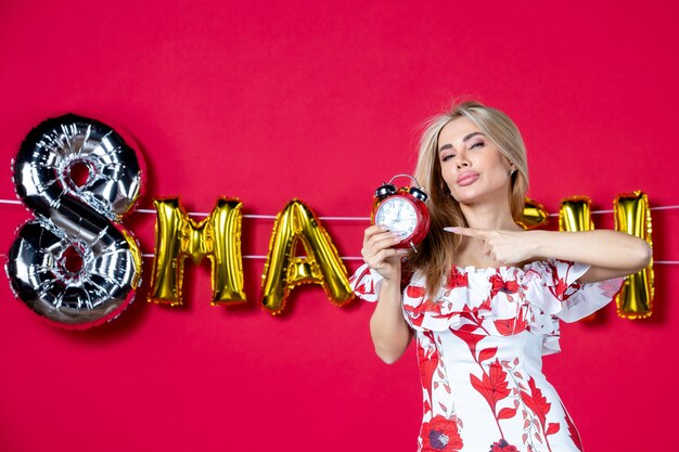 Front view young female in cute dress holding clock on reds time color