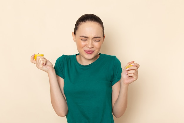 Front view young female in dark green shirt and blue jeans biting lemon on beige