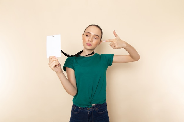 Front view young female in dark green shirt and blue jeans holding identity card on beige