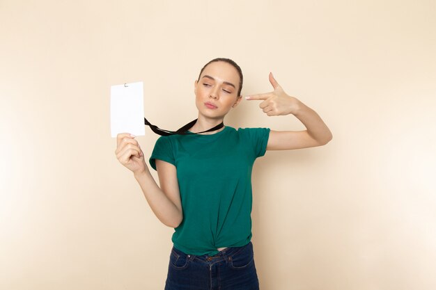 ダークグリーンのシャツとベージュのIDカードを保持しているブルージーンズの正面の若い女性