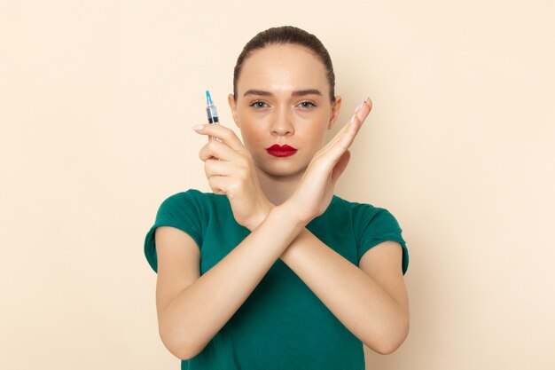 Front view young female in dark green shirt and blue jeans holding injection showing ban sign on beige