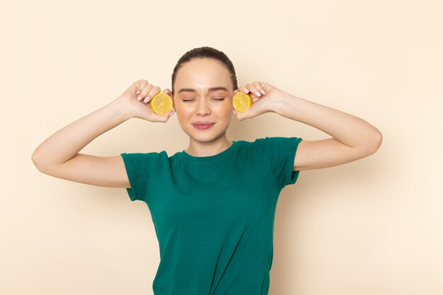 Front view young female in dark green shirt and blue jeans holding lemon slices on beige