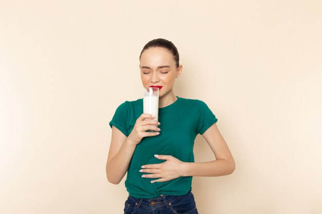 Front view young female in dark green shirt and blue jeans holding milk drinking on beige