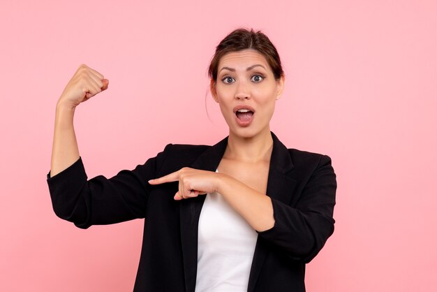 Front view young female in dark jacket flexing on pink background