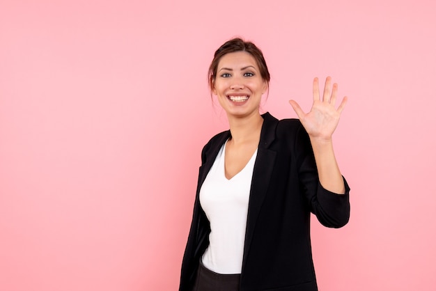 Front view young female in dark jacket greeting and smiling on pink background