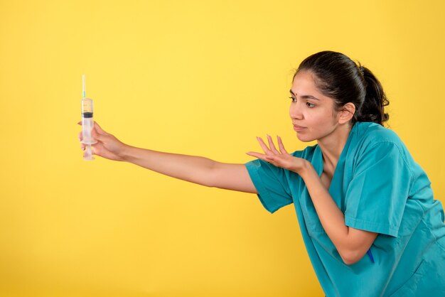 Front view of young female doctor giving syringe on yellow wall