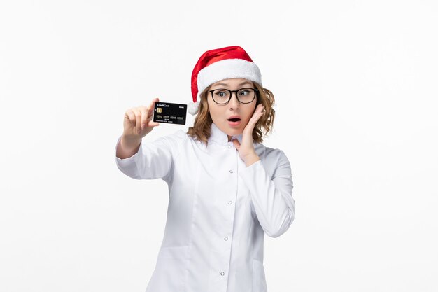 Вид спереди молодая женщина-врач, держащая банковскую карту на белой стене, праздничная медсестра, канун нового года