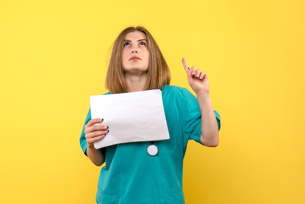 Front view of young female doctor holding files on a yellow wall