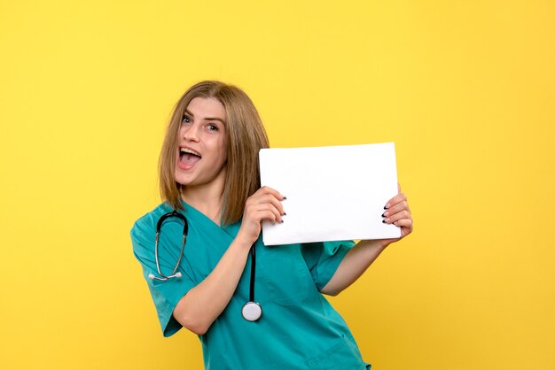 Front view of young female doctor holding files on yellow wall