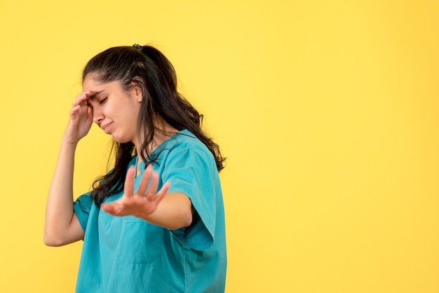 Foto gratuita vista frontale del giovane medico femminile che tiene la sua testa con dolore sulla parete gialla