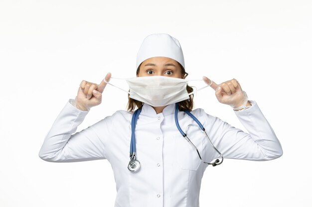 白い表面にコロナウイルスによる保護マスクを保持している正面図若い女性医師
