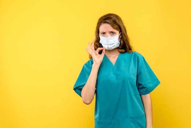 Вид спереди молодая женщина-врач в маске на светло-желтом пространстве
