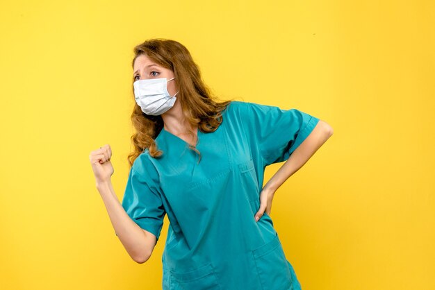 Front view young female doctor in mask on light yellow space