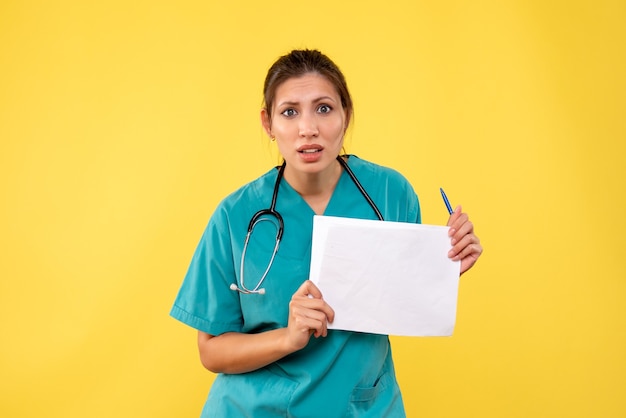 Front view young female doctor in medical shirt holding paper analysis on yellow background