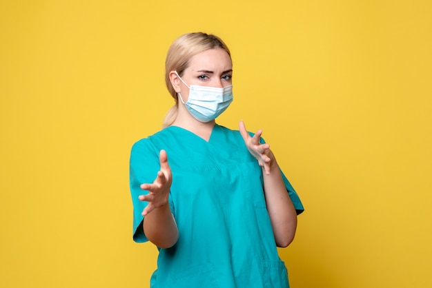 Front view of young female doctor in medical shirt and mask on the yellow wall