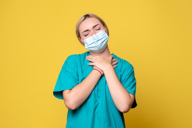 Вид спереди молодой женщины-врача в медицинской рубашке и маске на желтой стене