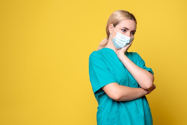 Front view of young female doctor in medical shirt and mask on yellow wall