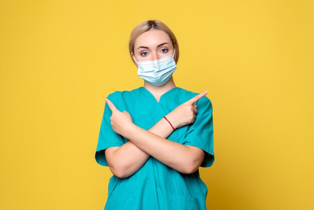 Front view of young female doctor in medical shirt and mask on yellow wall