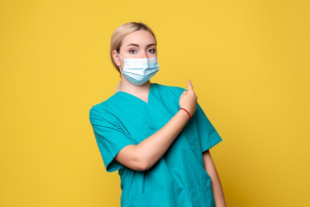 Вид спереди молодой женщины-врача в медицинской рубашке и маске на желтой стене